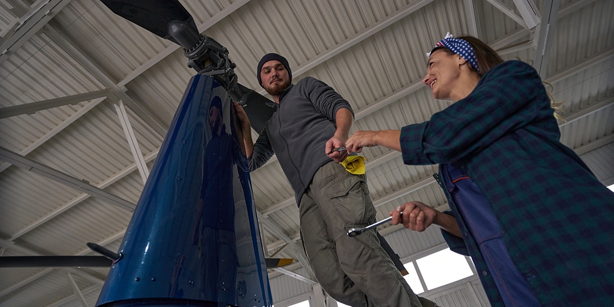 Caucasian man and woman mechanic in uniform using metal tools to repair helicopter rotors