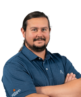 Portrait of a man with long hair and a beard wearing a blue polo shirt with a logo on the sleeve, arms crossed and smiling.